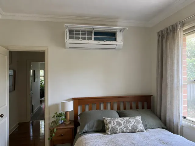 Open split system on a cream bedroom wall above a wooden bed, with clean filters visible in Enfield