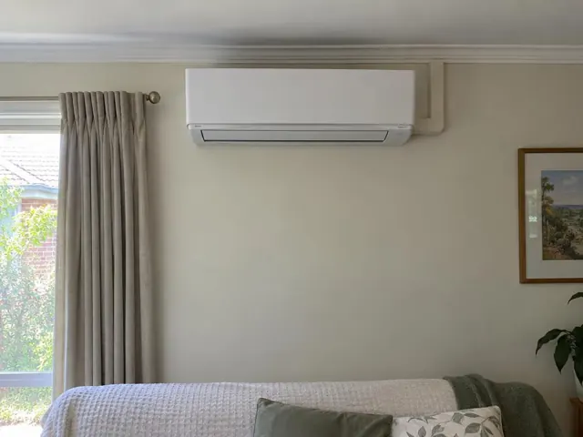 Wall-mounted split system above a bed in a beige bedroom with curtains and framed wall art in Broadview