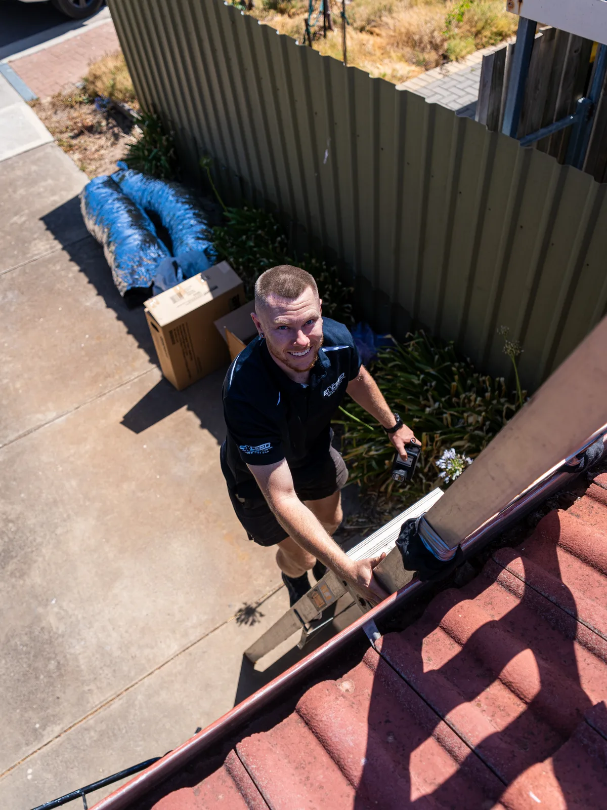 Technician climbing to the roof with ducting laid out below