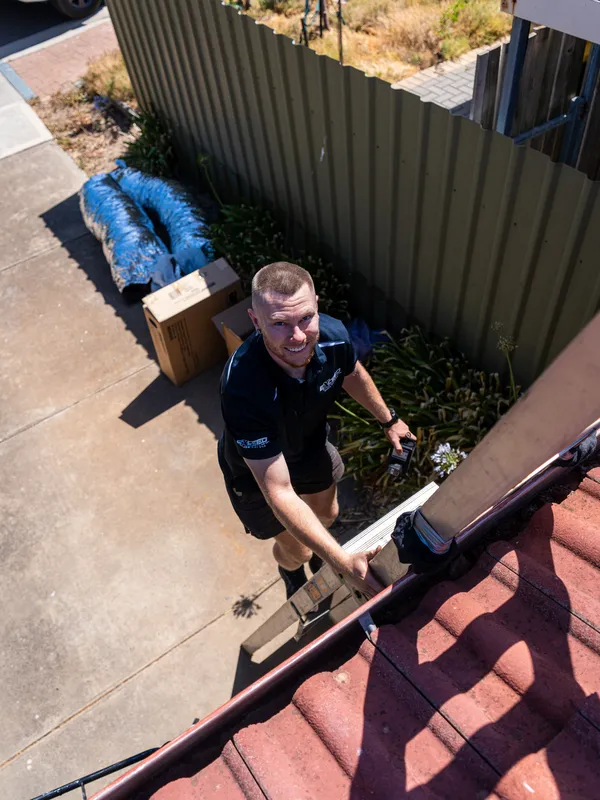 Technician climbing to the roof with ducting laid out below