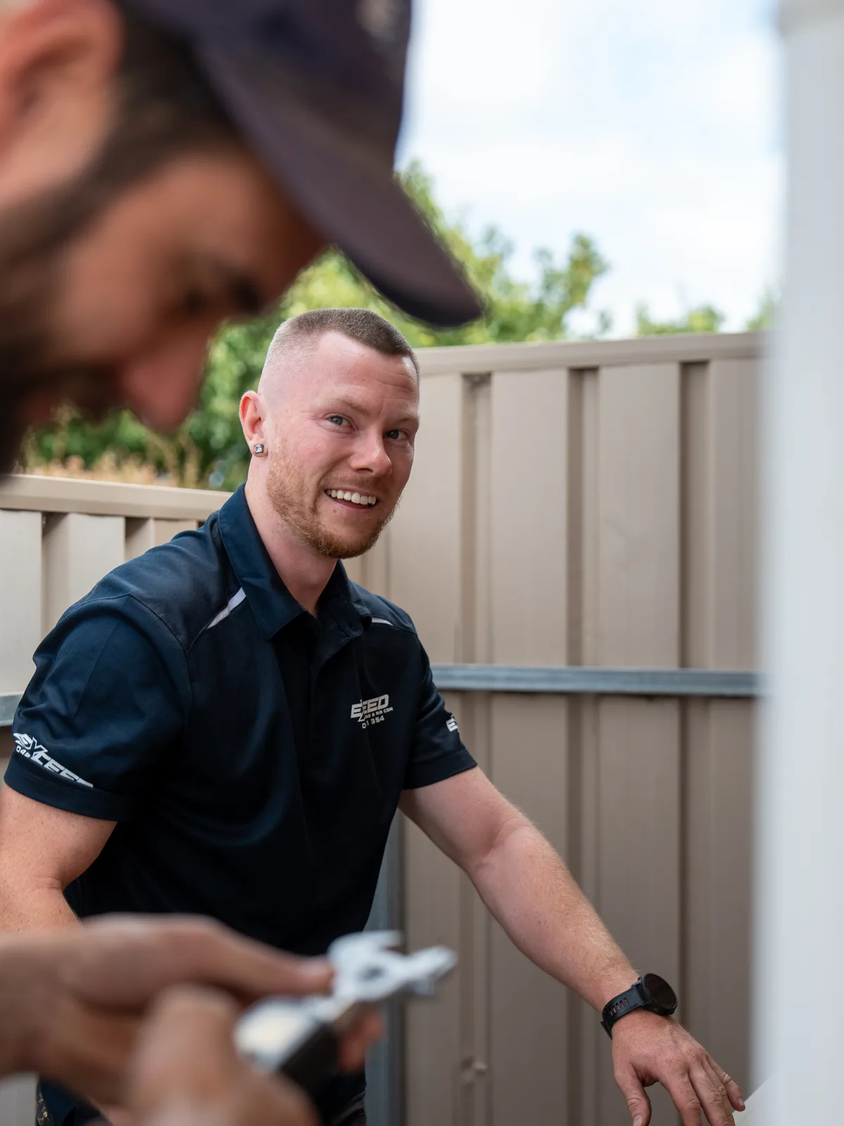 Smiling technician beside an outdoor unit at the side fence